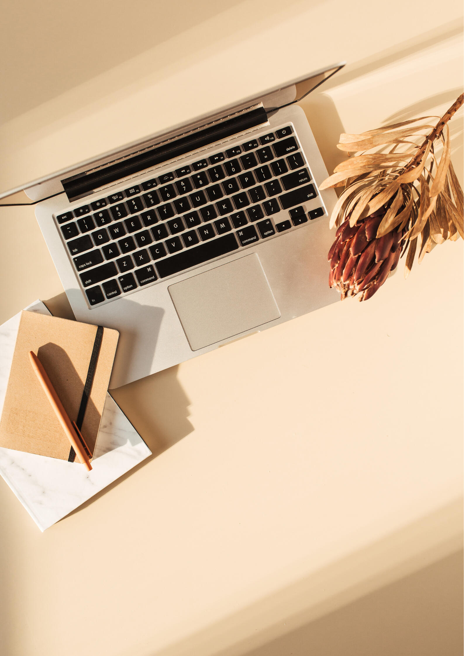 A laptop, notepad and pencil on a beige surface.